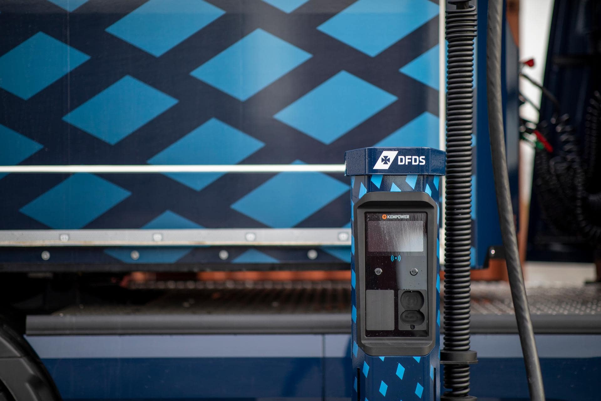 Electric truck loading station in two blue colour variants as livery, with an electric truck in the background