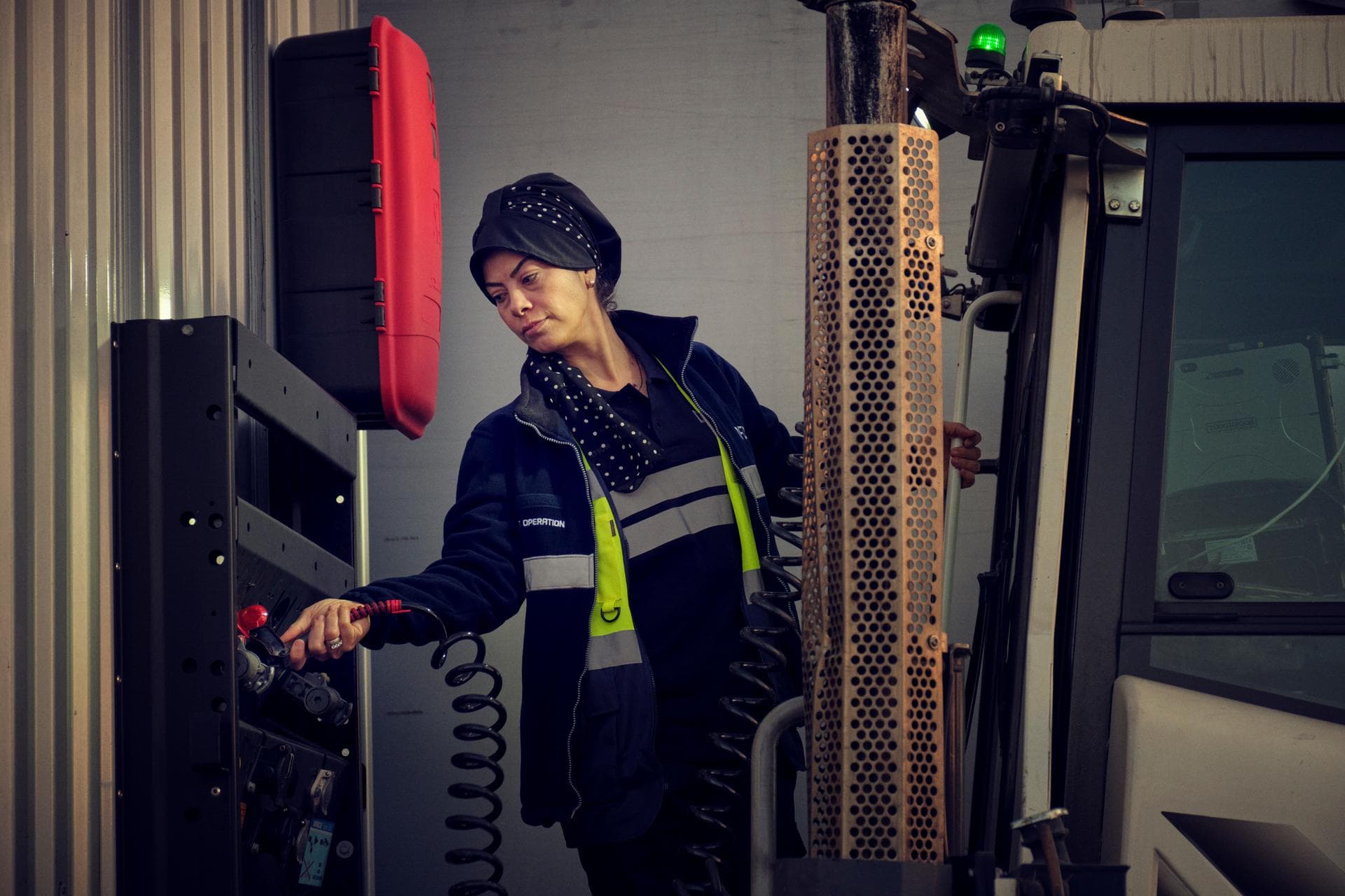 Operational staff warehousing and terminals: female worker in DFDS clothing, disconnecting the cable from a trailer, standing at the back of a tug master